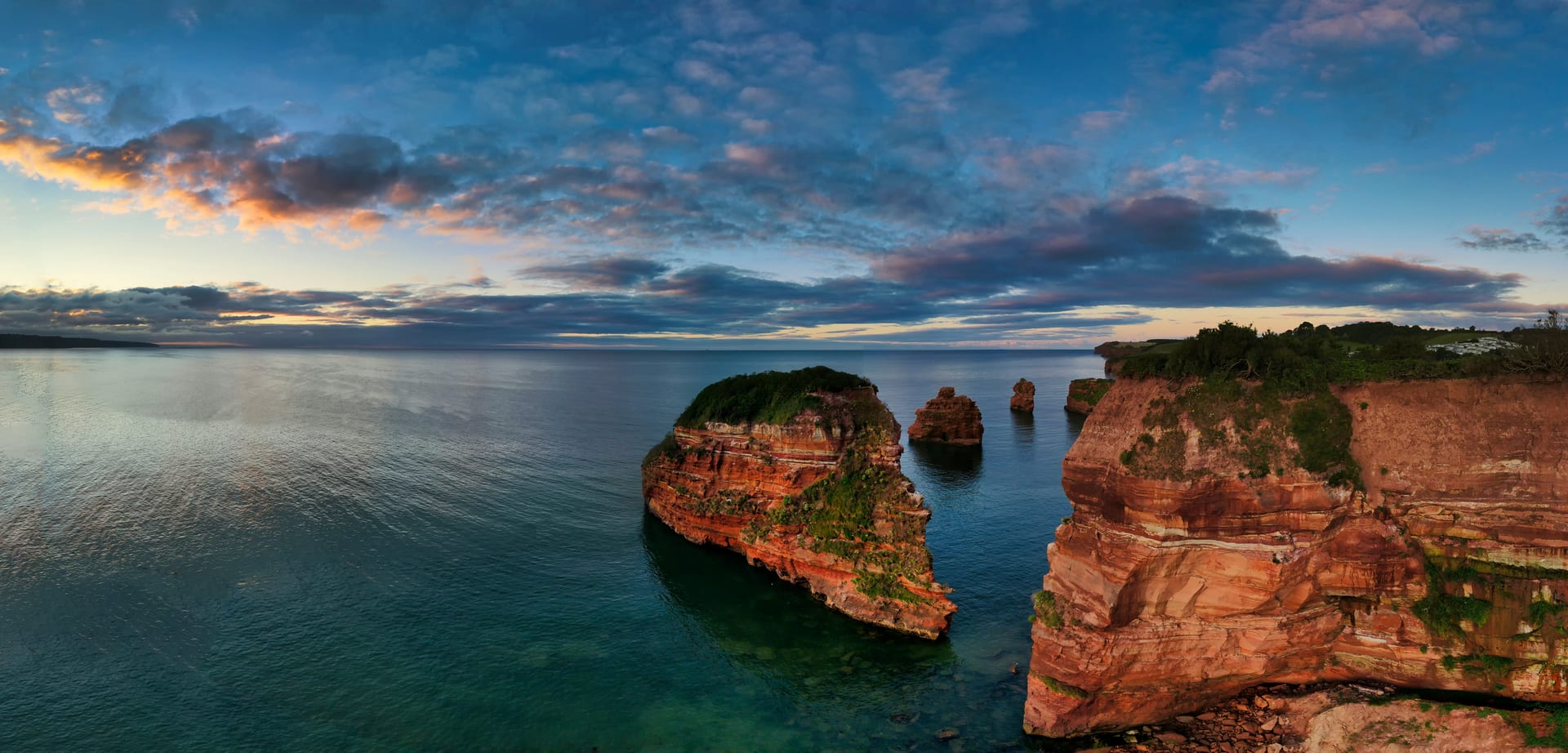 Red sandstone sea stacks and cliffs on a calm coastline at sunset
