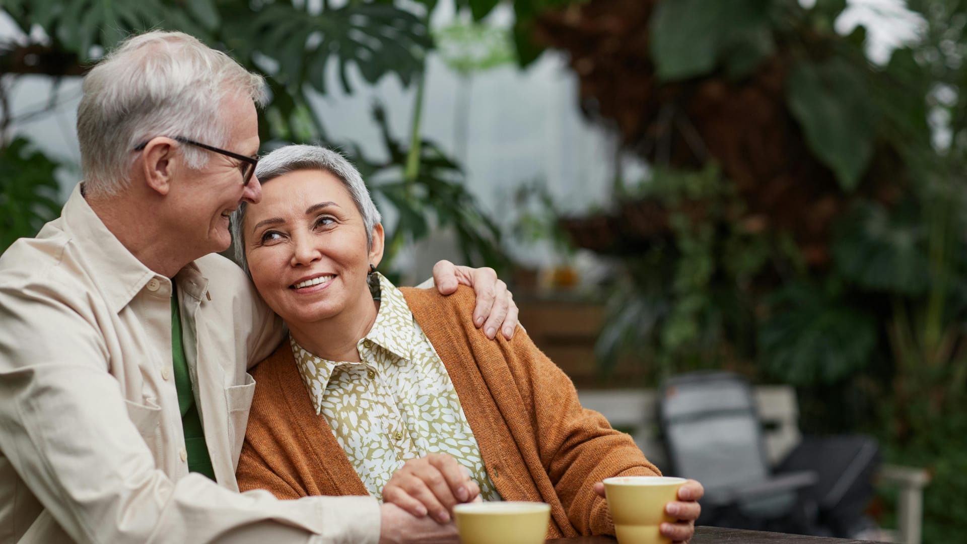 A senior couple sharing coffee at an outdoor table, smiling at each other