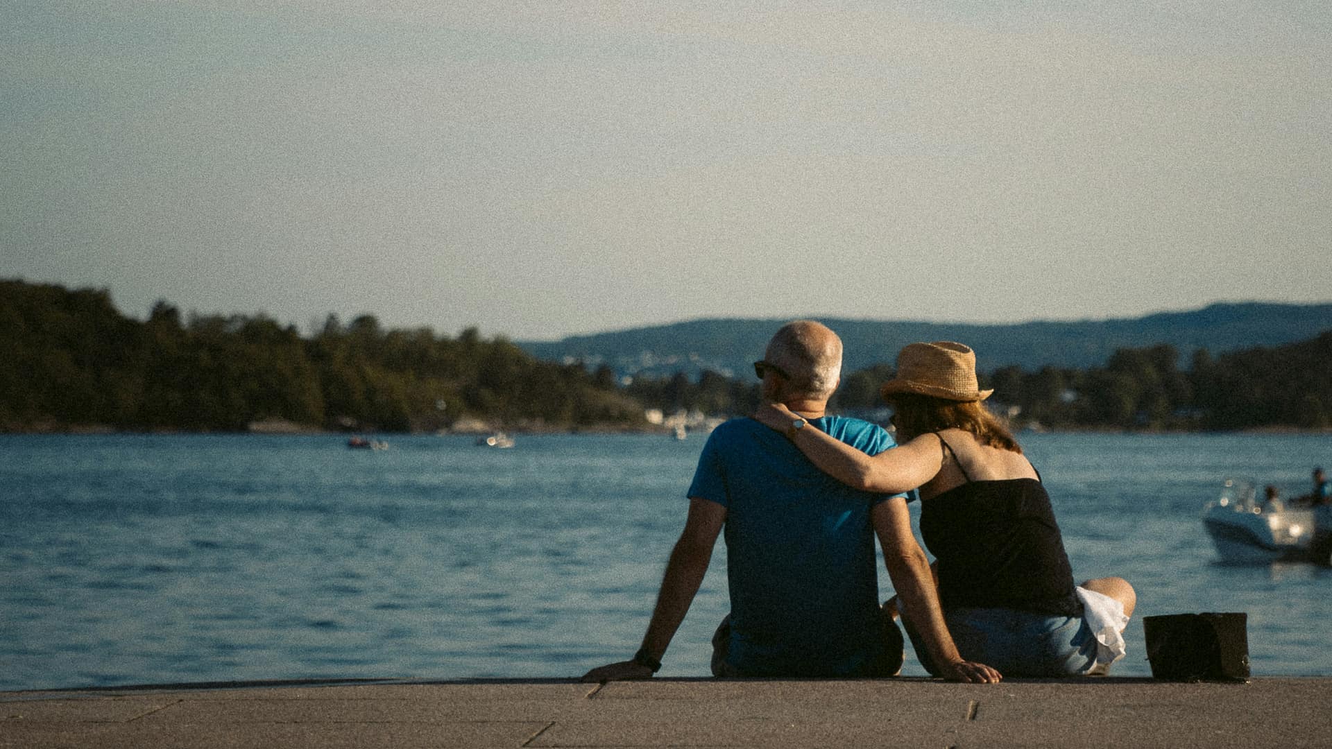 A couple sitting on a waterfront pier looking out across a bay